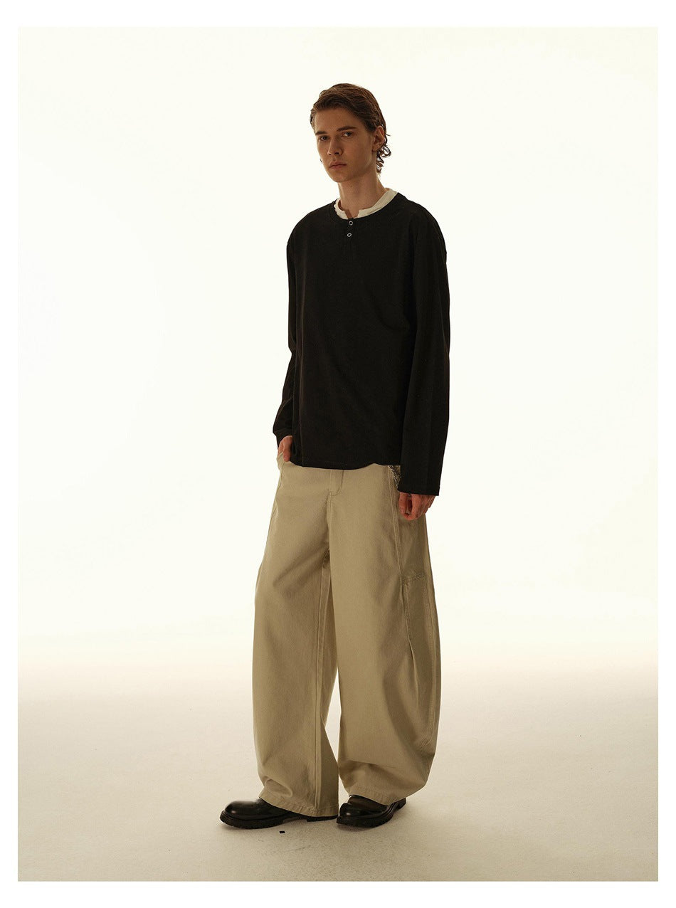 Full-length view of a man in a black long-sleeve henley top with white collar, wide khaki pants and black boots