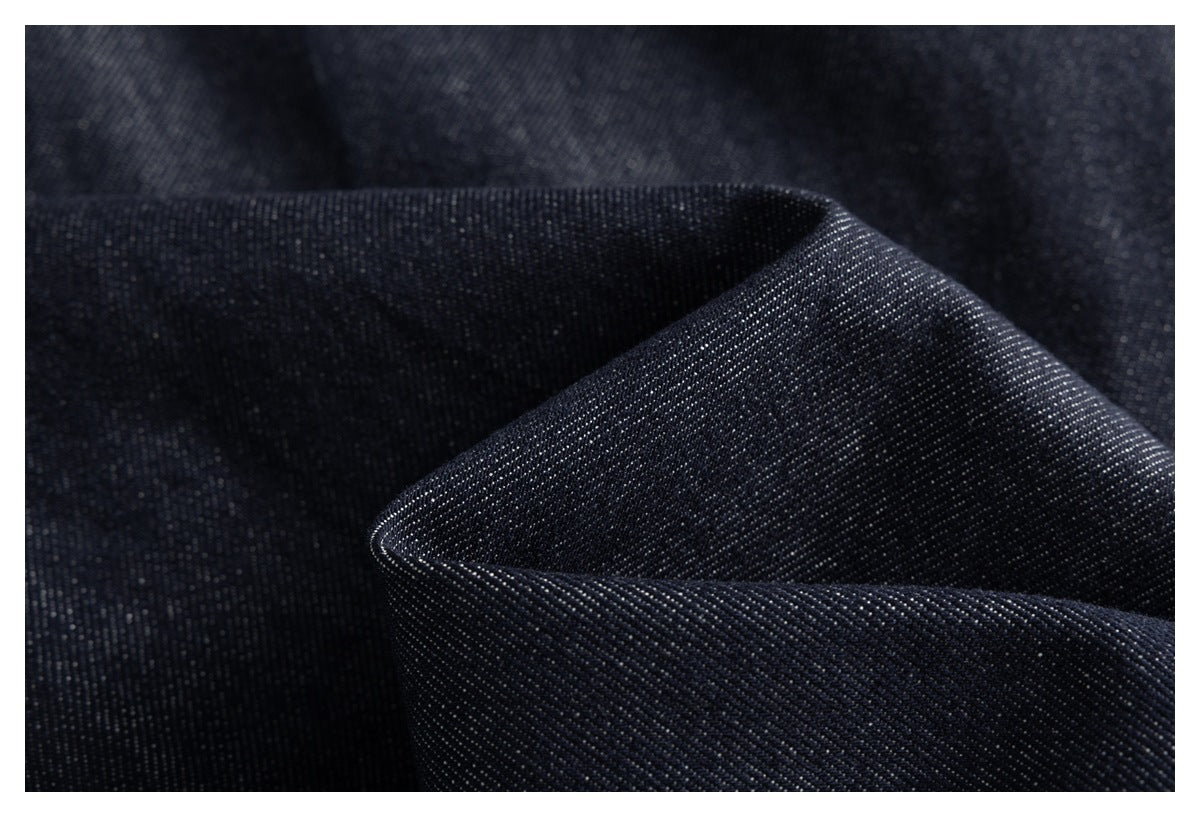 Macro view of dark indigo trouser fabric folded to show its fine diagonal weave.