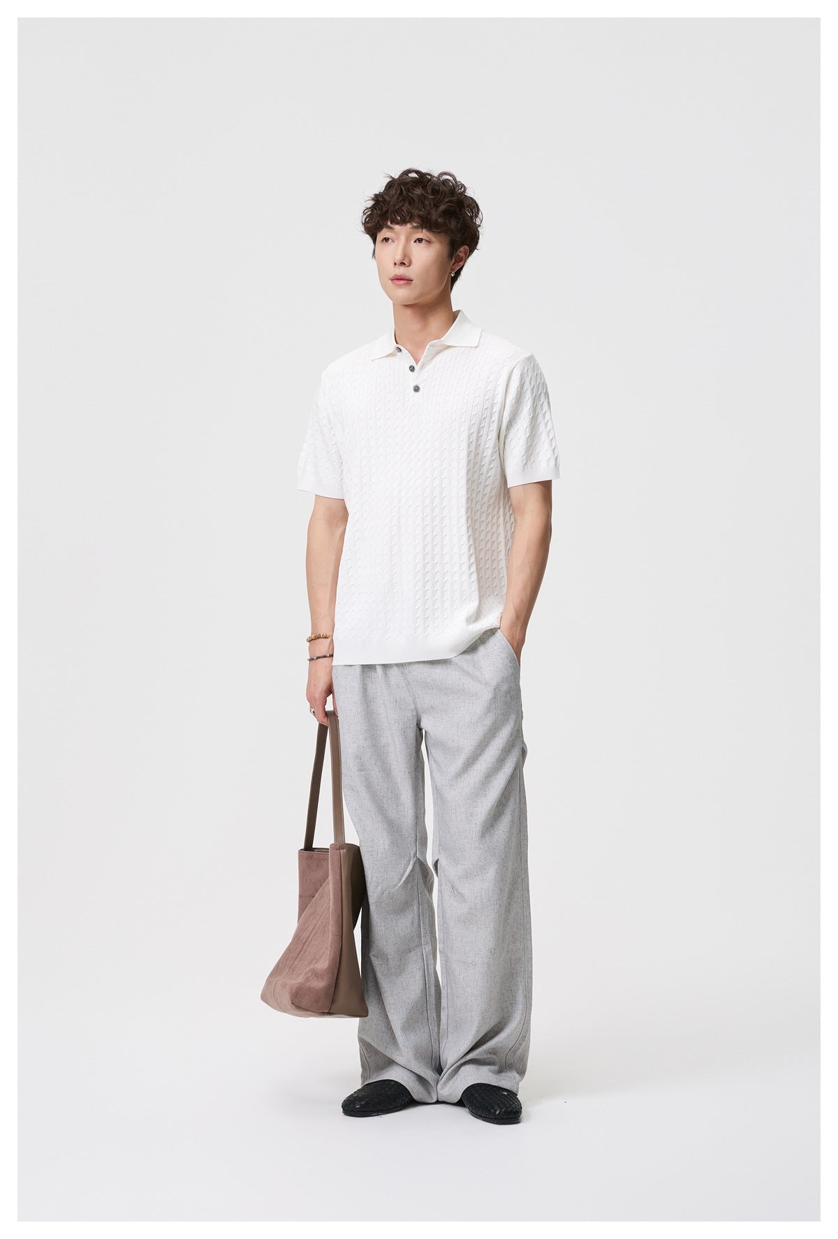 Model wearing a white short-sleeve cable-knit polo with gray trousers, shown full length from the front.