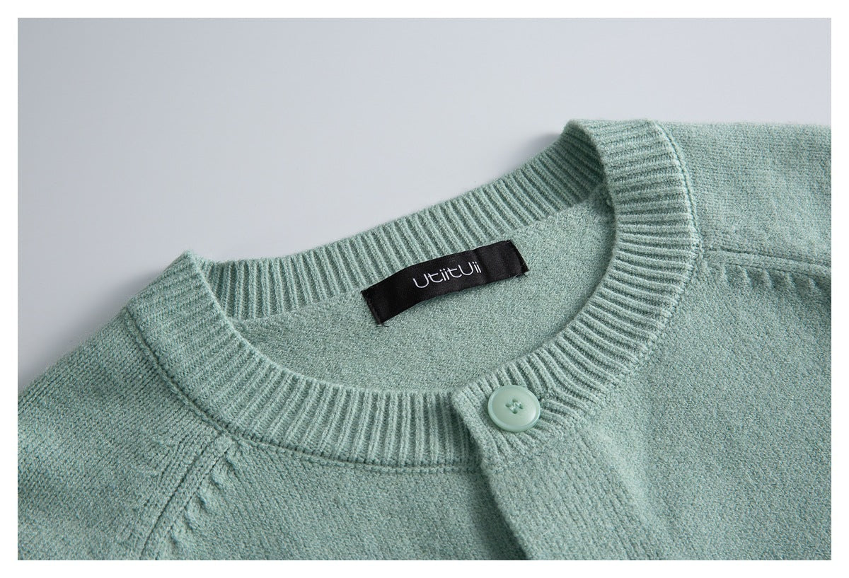 Close-up of a pale mint-green knit cardigan collar, button, and sewn-in neck label.