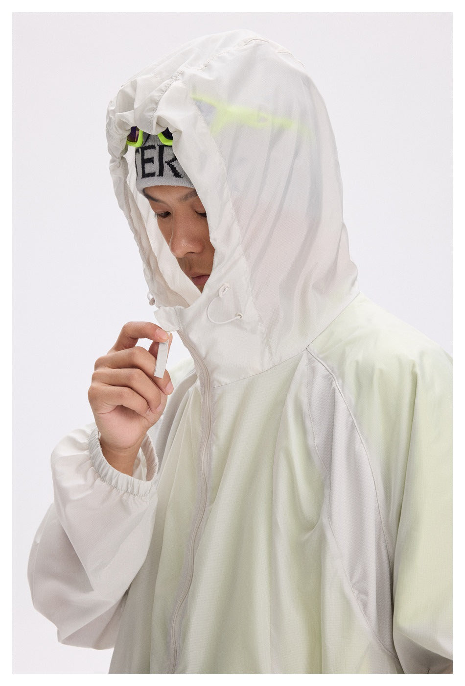 Close view of a model in the pale mint and white jacket, raising its hood and adjusting the drawcord.