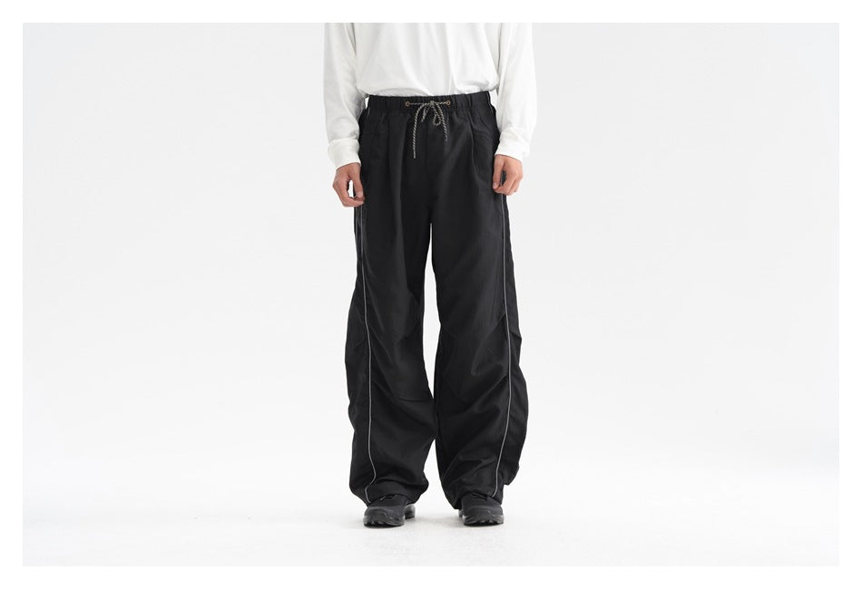 Front view of a model wearing black loose-fit drawstring pants with light-colored side piping.