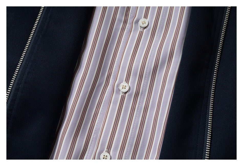 Close-up of a light striped button-front shirt framed by a dark jacket with metal zippers.