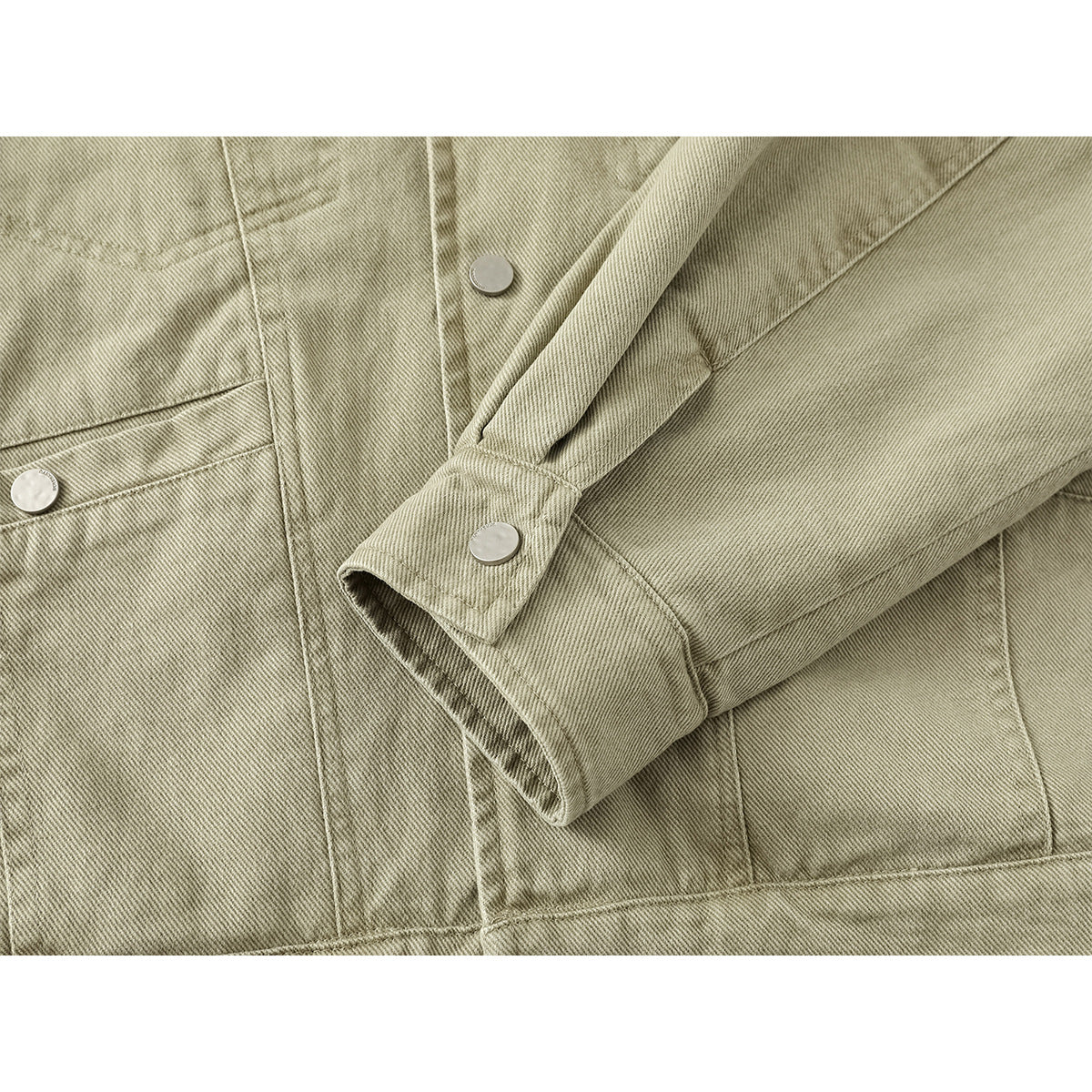 Close-up of a khaki jacket sleeve cuff with a snap, plus flap pockets and panel stitching.
