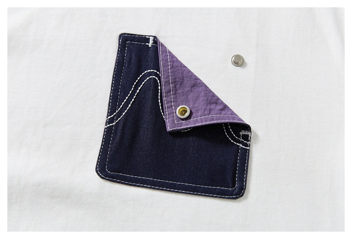 Close-up of the T-shirt's indigo pocket with white stitching, a folded purple flap, and metal snap fasteners.