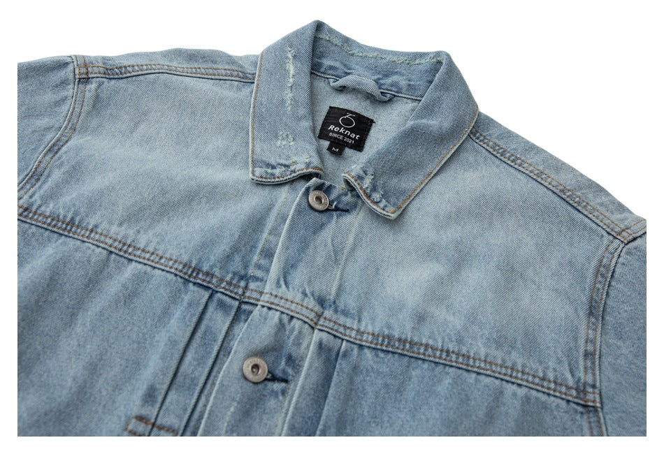 Close-up of a light blue denim jacket collar, buttons, chest yoke, and sewn neck label.