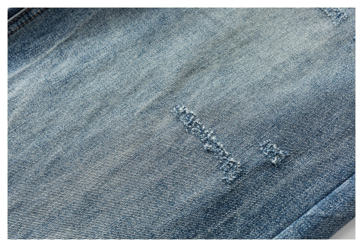 Close-up of light blue washed denim with small distressed marks and visible diagonal twill texture.