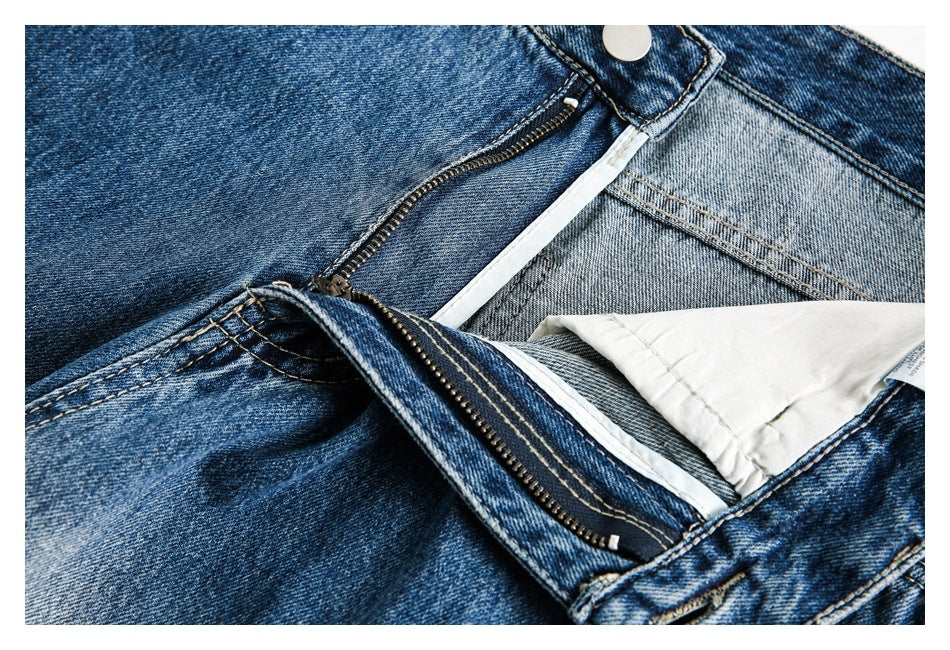 Close-up of blue washed jeans with the zipper fly open, showing the inner waistband and white pocket lining.