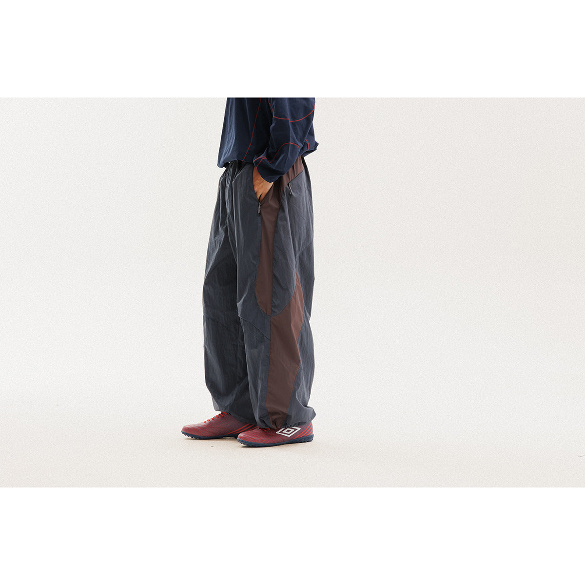 Cropped side view of a model wearing loose charcoal pants with brown side panels and red-accented shoes.