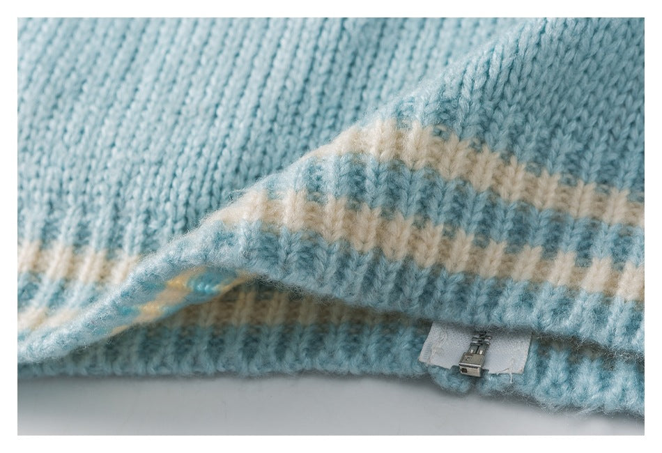 Close-up of pale blue knitted sweater fabric with a cream stripe and a small zipper fastening.