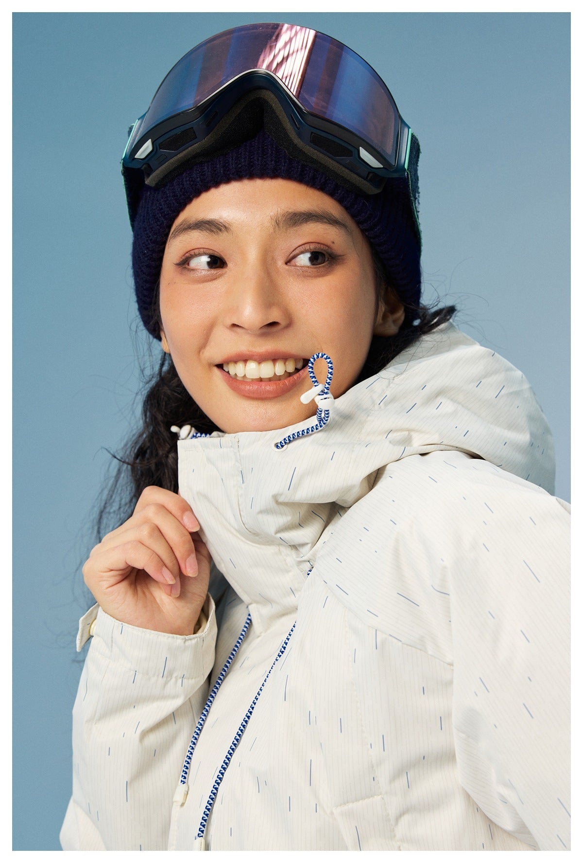 Close-up of the white jacket's fine blue dash pattern, hood, and blue-and-white drawcord beside the model's face.