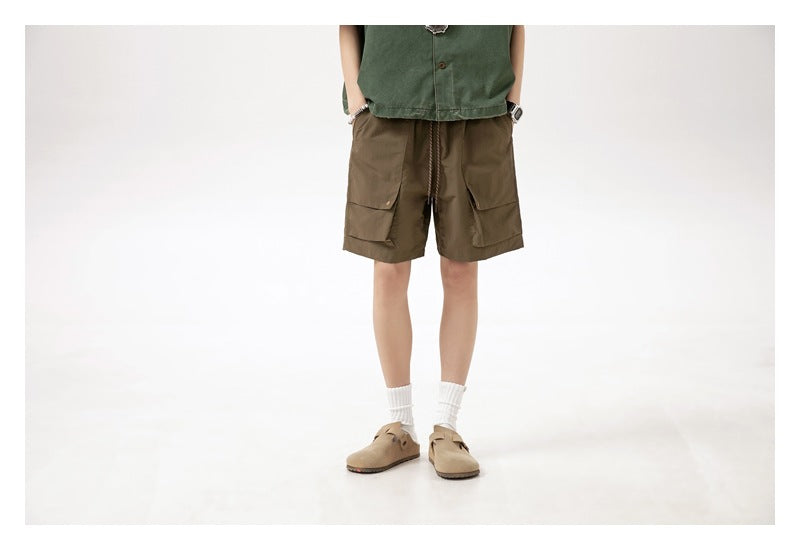 Cropped front view of a model wearing brown cargo shorts with large flap pockets and a drawstring waist.