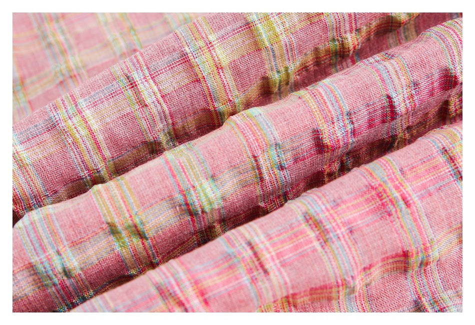 Close-up of textured pink plaid fabric gathered into folds, with multicolor stripes.