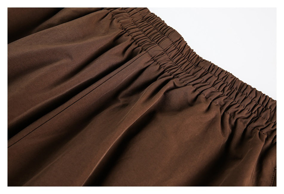 Close-up of the gathered elastic waistband and pleats on brown track pants.