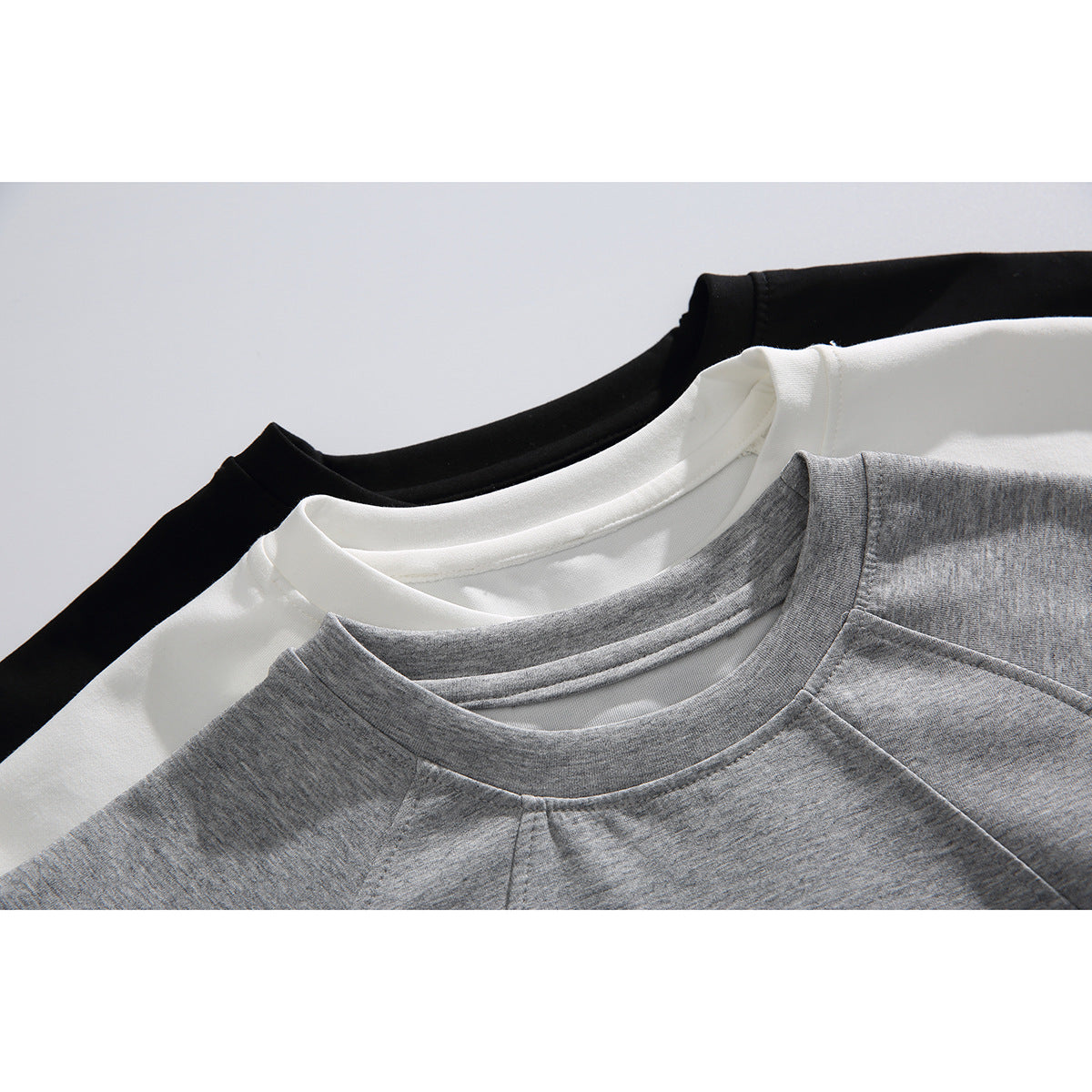 Close-up of gray, white, and black crewneck tops, showing the collars and raglan shoulder seams.