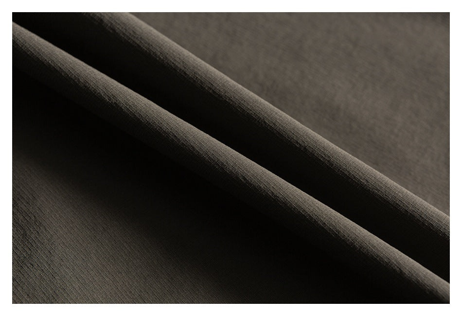 Close-up of olive-gray garment fabric arranged in soft folds, showing its fine surface texture.