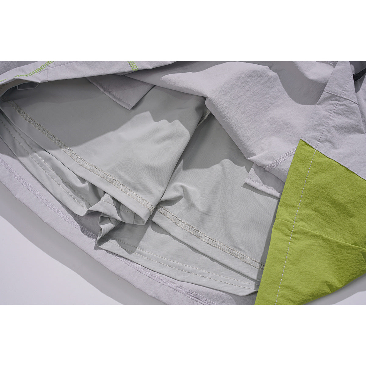 Inside view of light gray shorts showing seam finishing, lining, and a lime-green contrast panel.