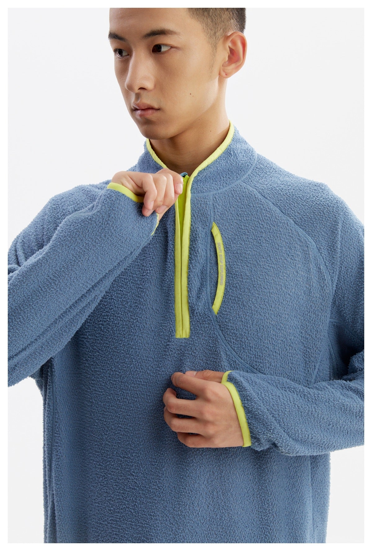 Close-up of a model wearing a blue textured pullover with a stand collar, lime trim, and a short zip front.