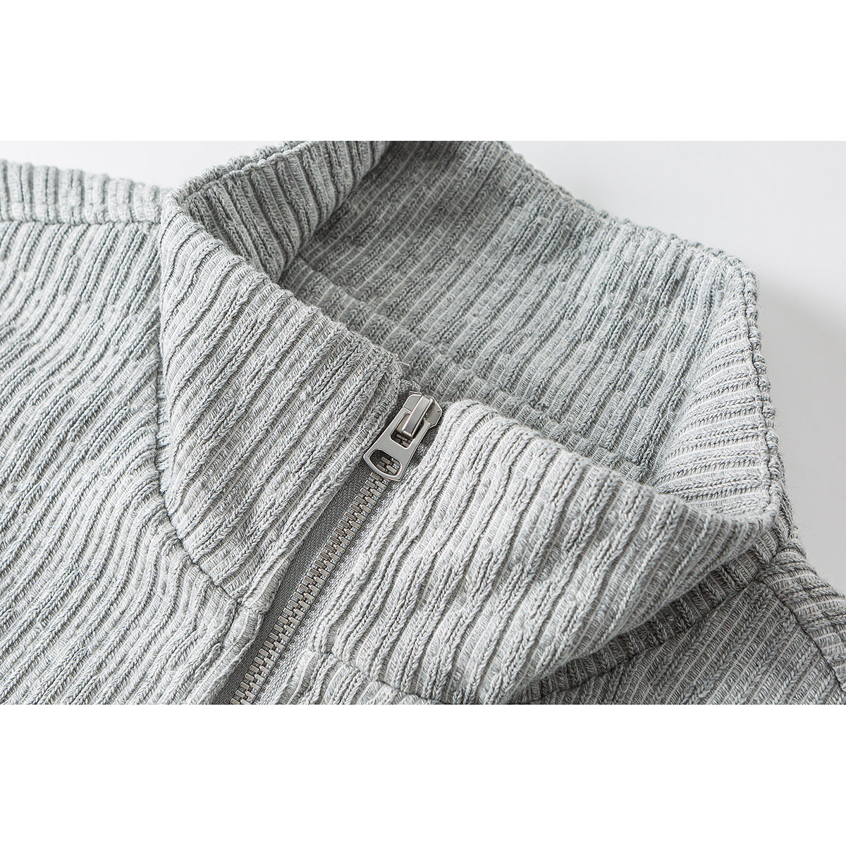Close-up of a light gray ribbed jacket's high collar and silver front zipper.