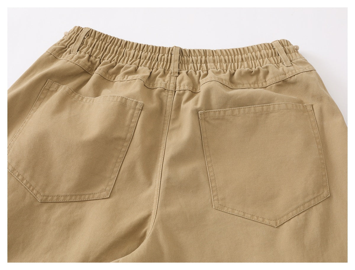 Cropped rear view of tan pants with an elastic waistband, belt loops, and two patch pockets.