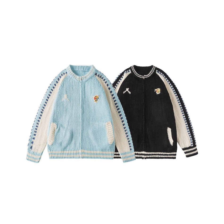 Two front views of knit zip cardigans in pale blue and black, both with cream sleeves and patterned stripe details.