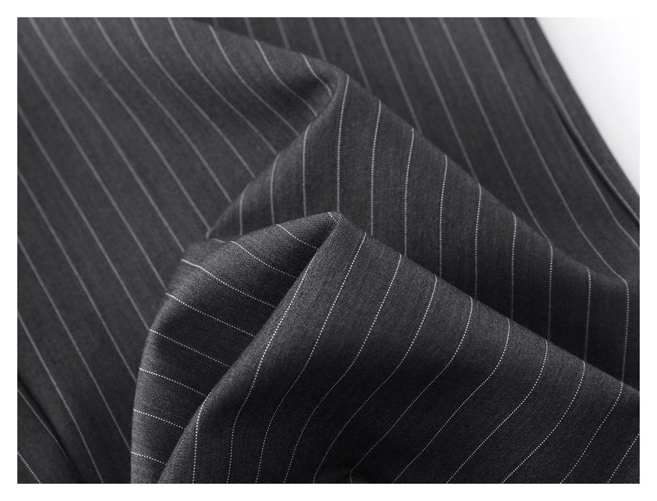 Close-up of charcoal trouser fabric with narrow light pinstripes and folded layers.