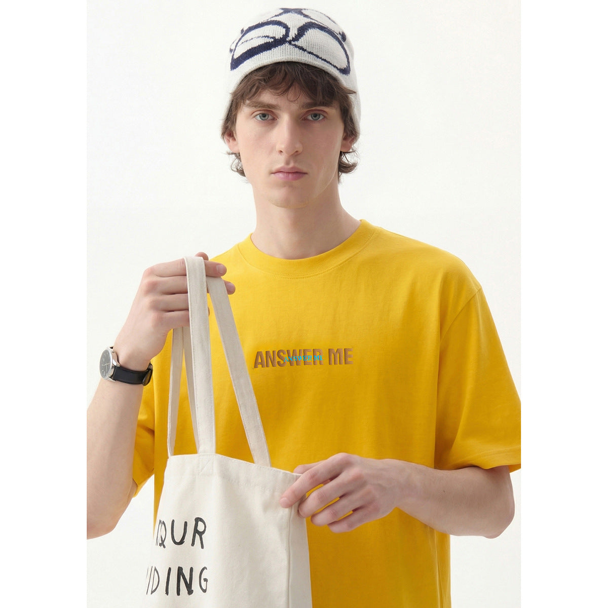 Close front view of a model wearing a yellow T-shirt with raised chest lettering.
