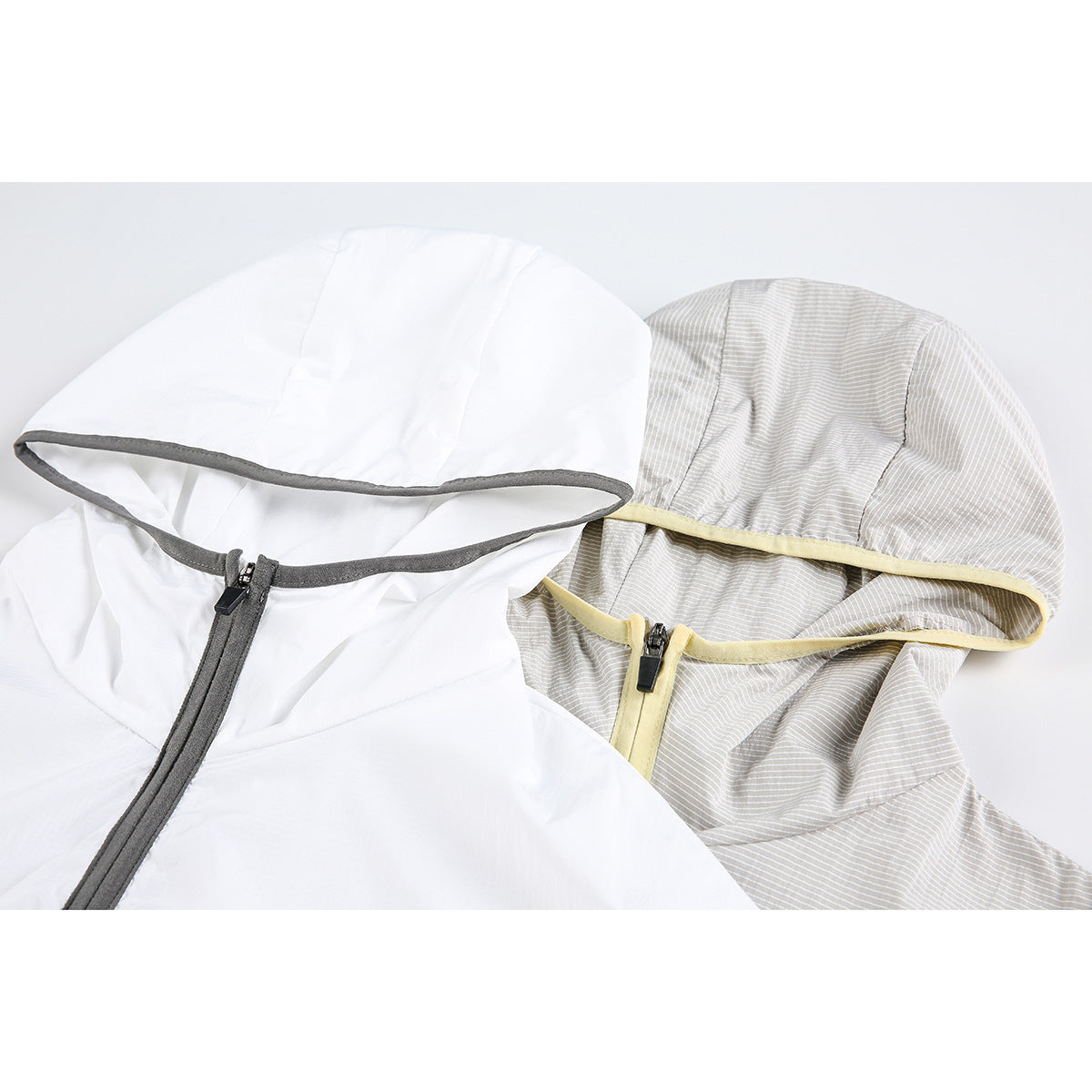 Close-up of two hooded jacket hoods with contrasting trim and front zippers, one white and one light gray striped.
