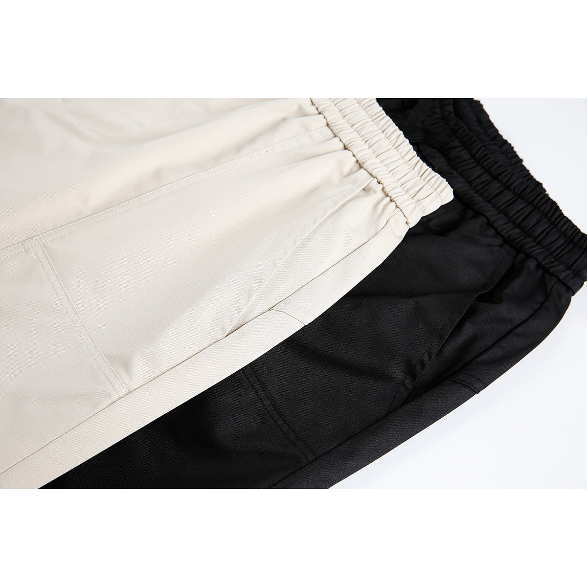 Close-up of beige and black pants showing elastic waistbands, front seams, and pocket stitching.