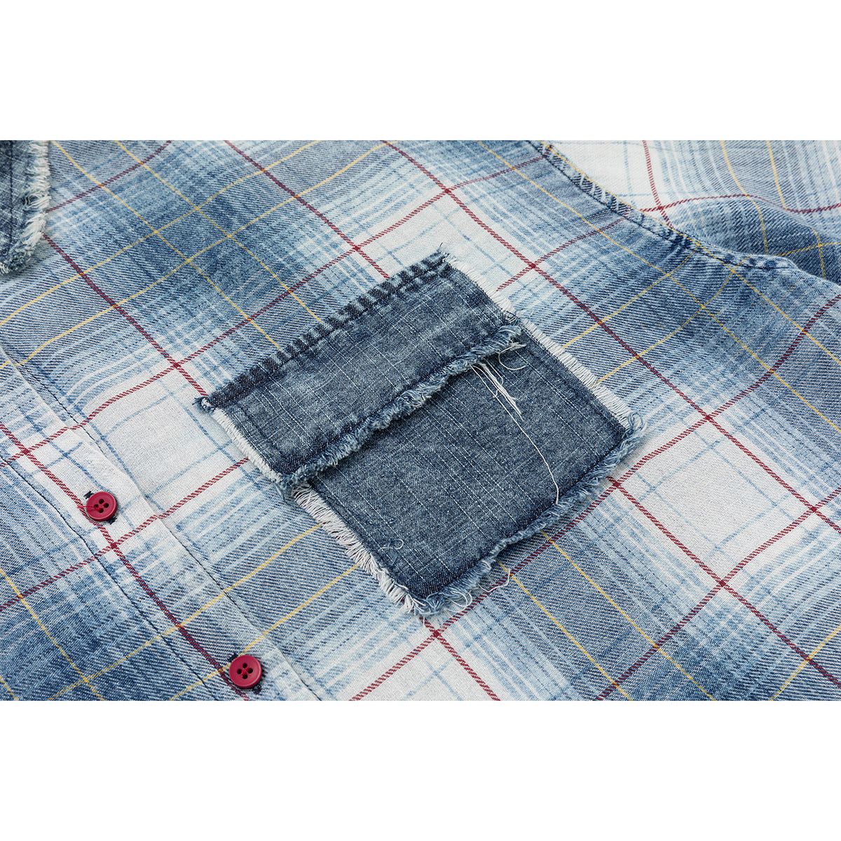 Close-up of the shirt’s blue plaid fabric, dark denim patch pocket with frayed edges, and red buttons.