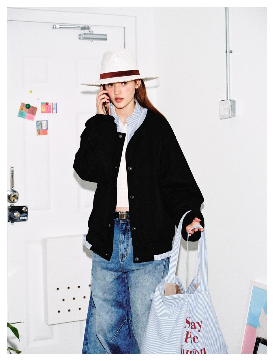 Model wearing a black snap-front jacket with a striped collar and hem peeking out, holding a striped tote.