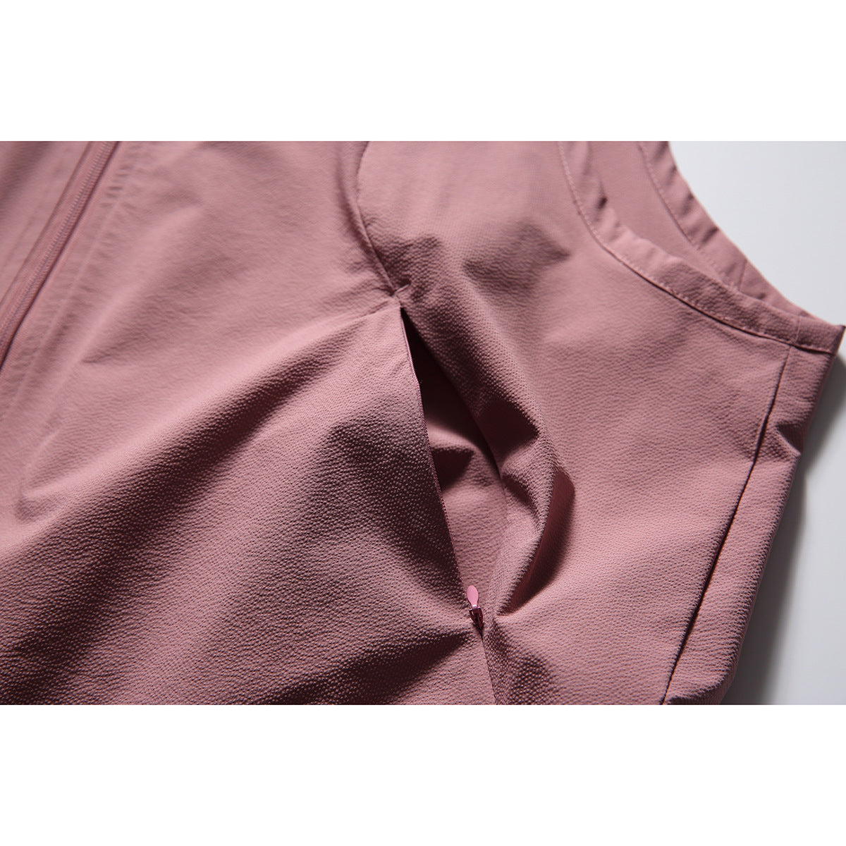 Close-up of the dusty rose vest's side seam and zippered pocket, with the textured fabric visible.