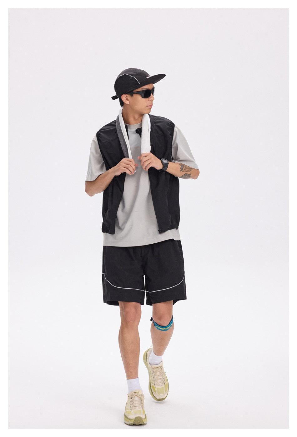 Model wearing a black sleeveless vest over a light gray T-shirt and black shorts with white piping.