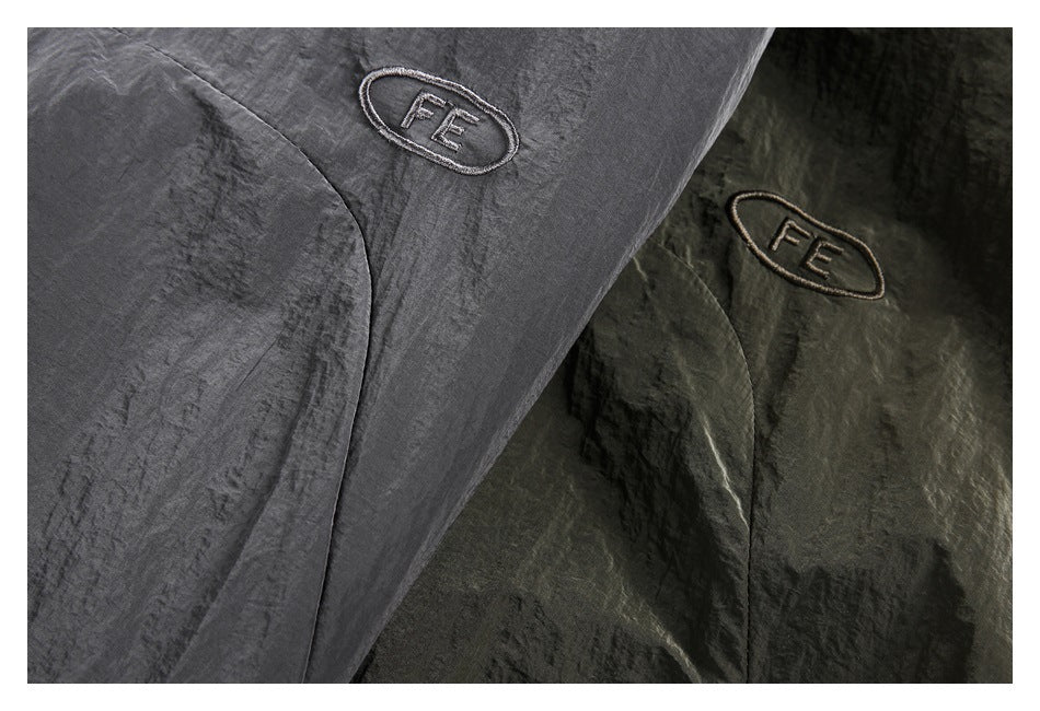 Close-up of embroidered oval FE emblems on charcoal gray and dark olive jacket fabric.