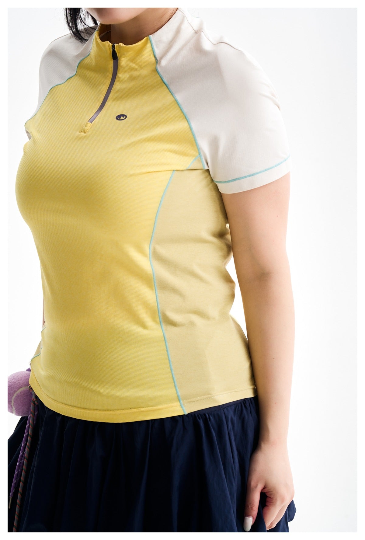 Model wearing a yellow quarter-zip top with white short sleeves and turquoise seam piping.