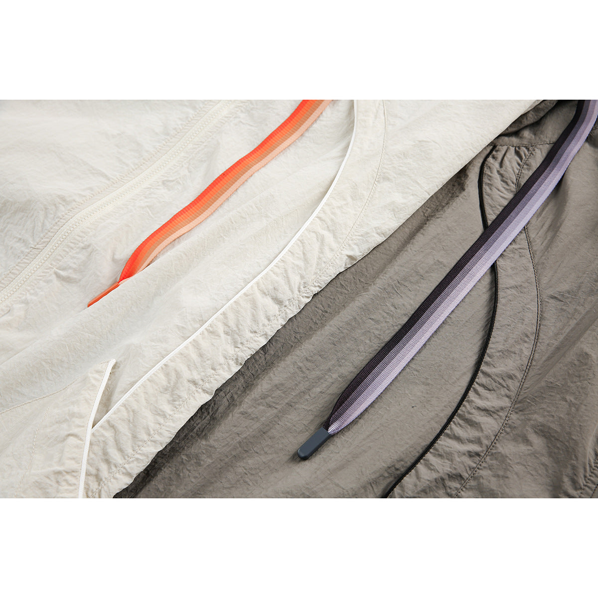 Close-up of ivory and gray jacket drawstrings and front fabric, with orange and lavender trim.