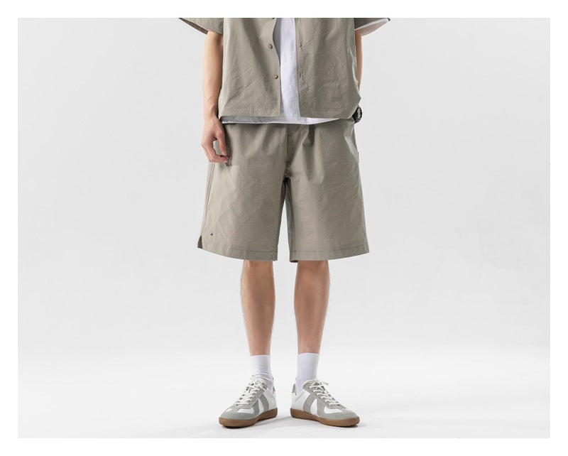 Cropped model facing forward in a taupe short-sleeve button shirt and matching knee-length shorts.