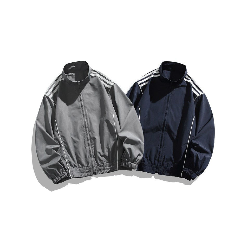 Two zip-front track jackets shown from the front: one gray and one navy, both with white shoulder stripes and elastic hems.