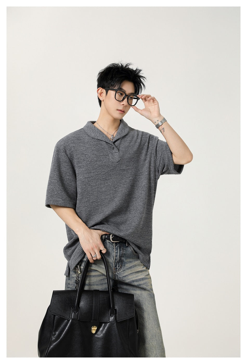 Model in a gray textured short-sleeve polo and faded jeans, carrying a large black handbag.