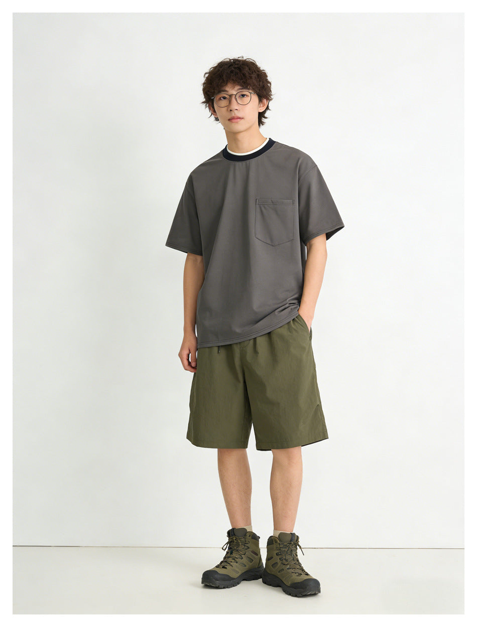 Model standing in a dark gray pocket T-shirt with navy collar, olive green shorts and hiking boots, front view