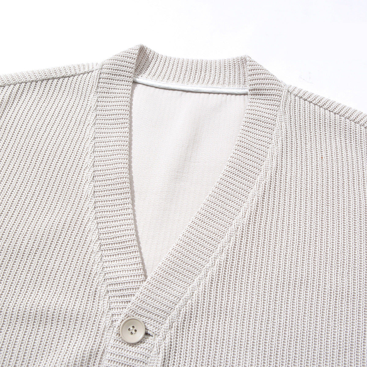 Close-up of a light beige ribbed cardigan showing its V-neck, button placket and collar.