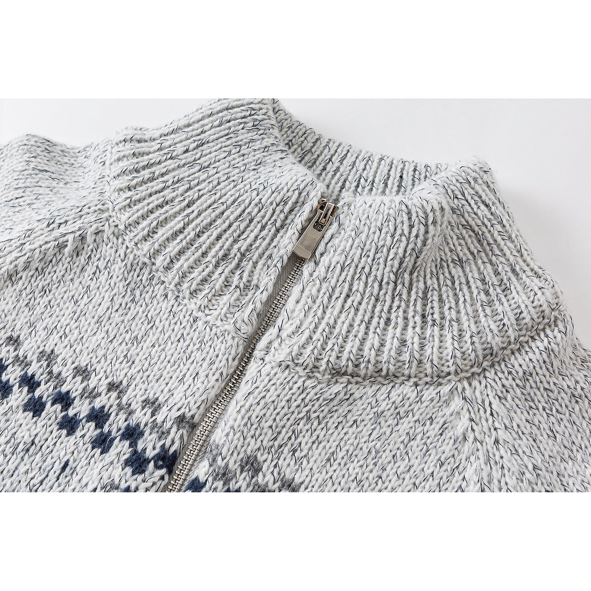 Close-up of a light gray knit sweater's ribbed stand collar and metal zipper, with a navy pattern at the edge.