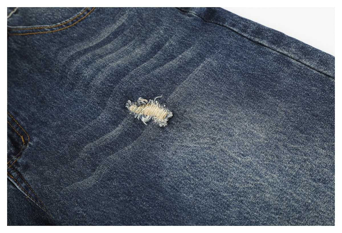 Close-up of faded dark blue denim with a small frayed tear and visible diagonal wear marks.