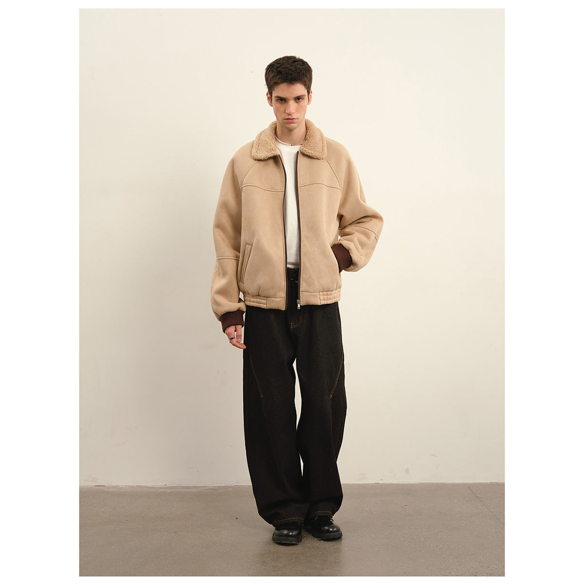 Front view of a model wearing a beige zip jacket with a plush collar, dark cuffs, and loose black trousers.