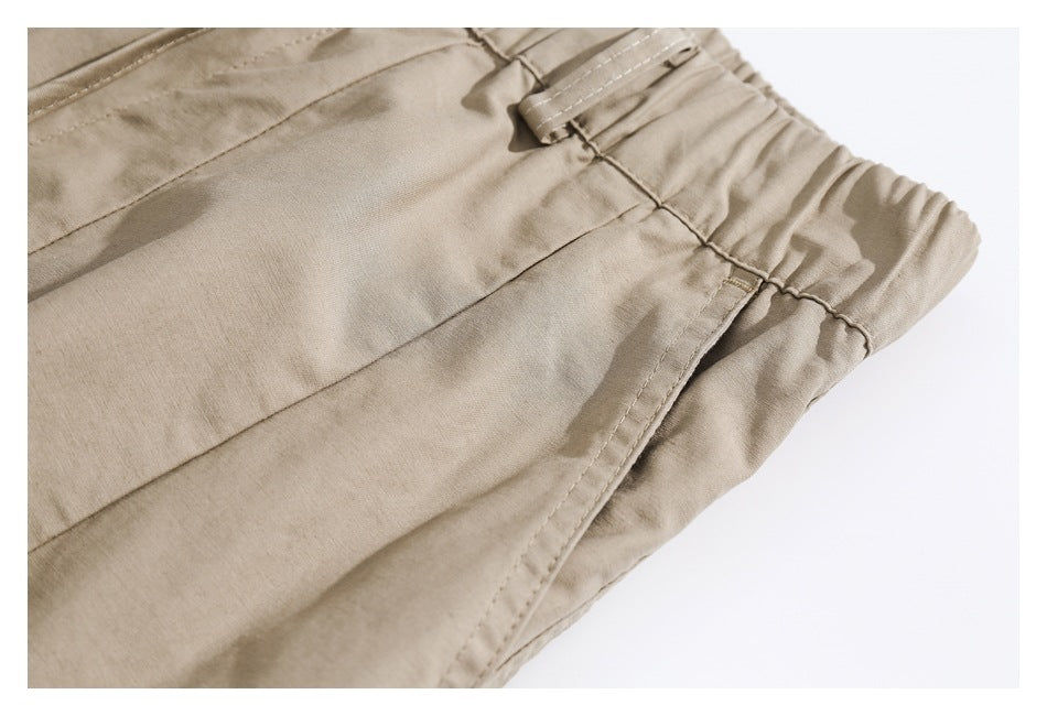 Close-up of beige pants showing the elastic waistband, belt loop, and stitched pocket edge.