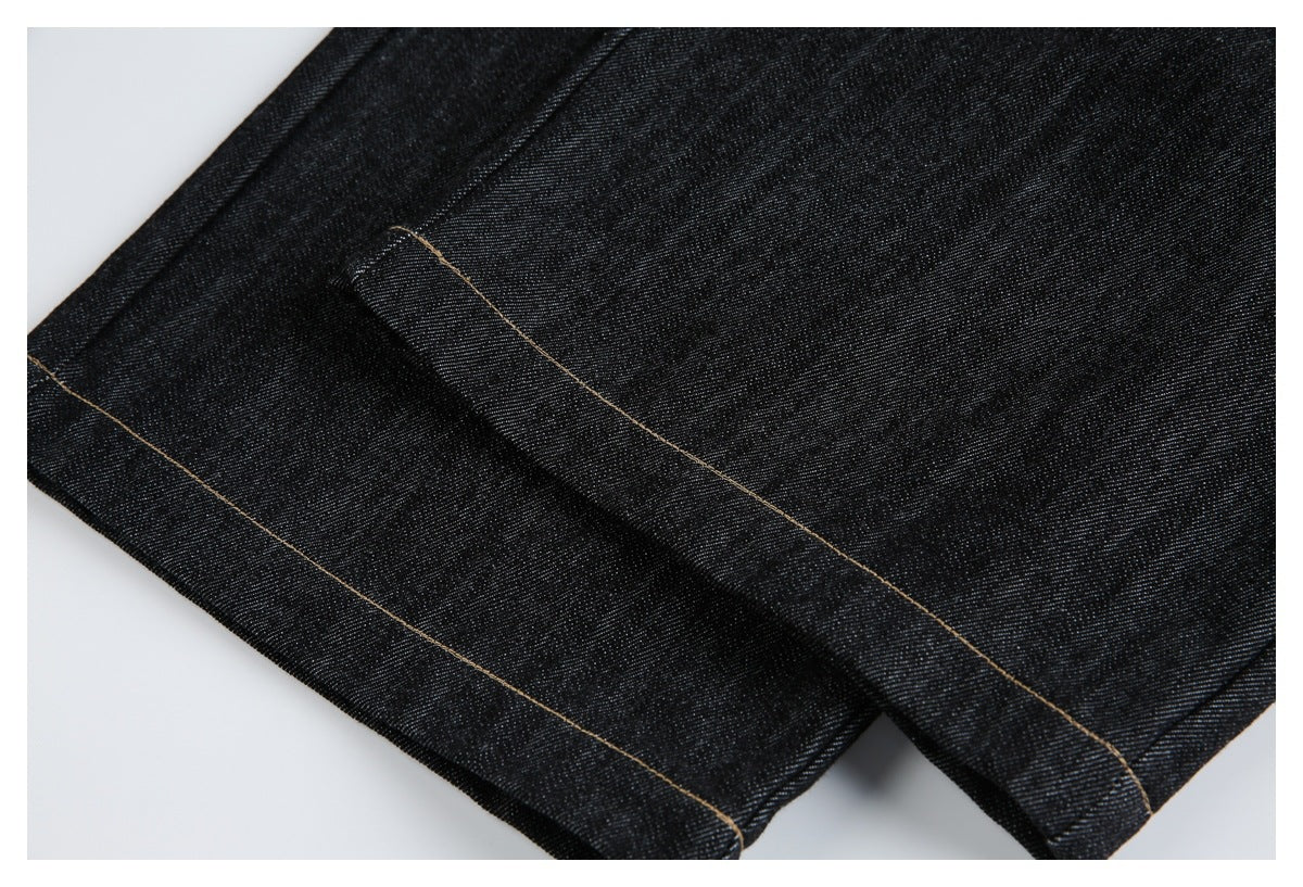 Close-up of a black denim jeans hem with parallel tan stitching.
