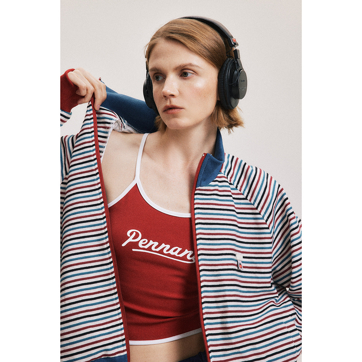 Close-up of a model in a red, blue and white striped zip jacket over a red top with white script.