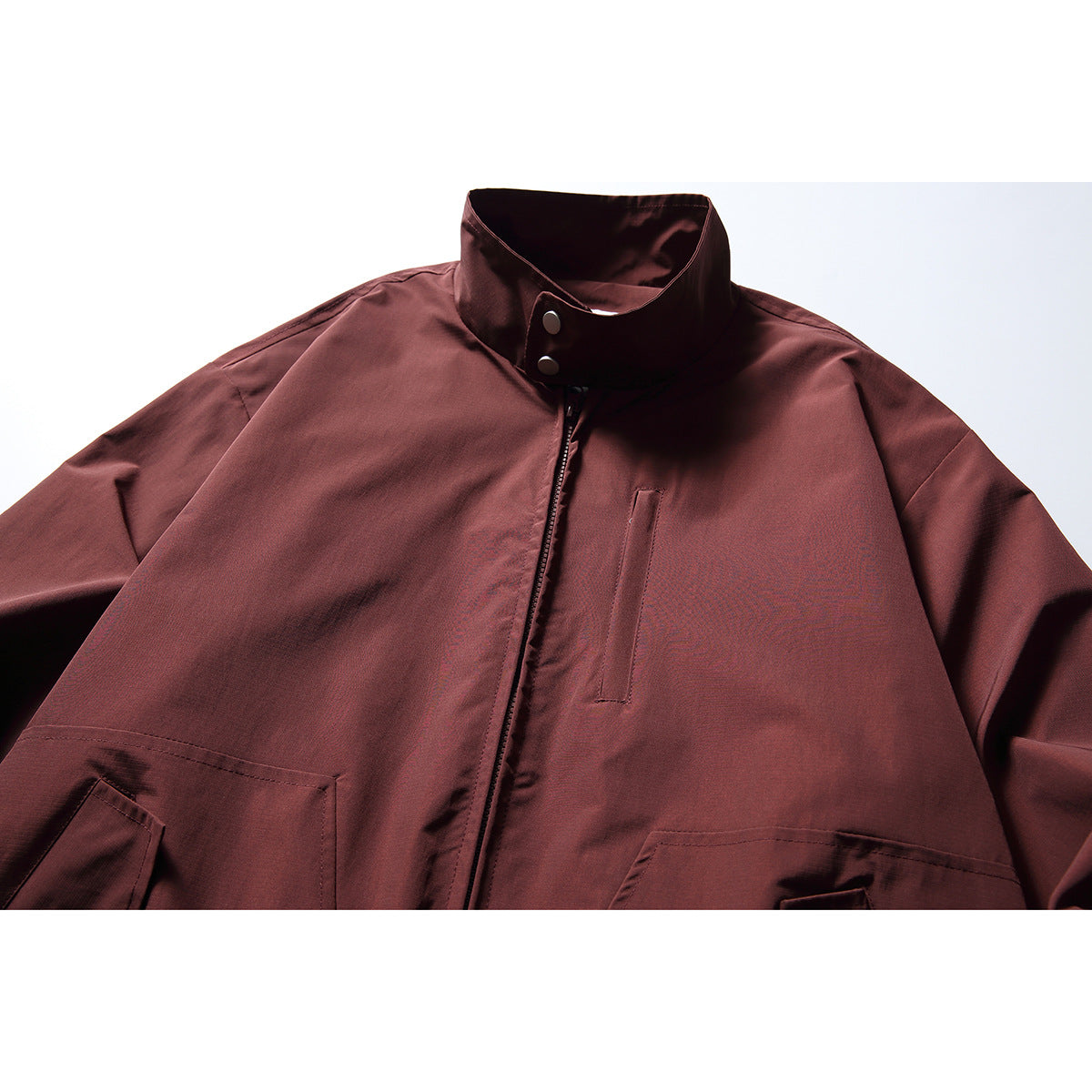 Close-up of a burgundy jacket front with a stand collar, snap closure, vertical chest pocket and flap hand pockets.
