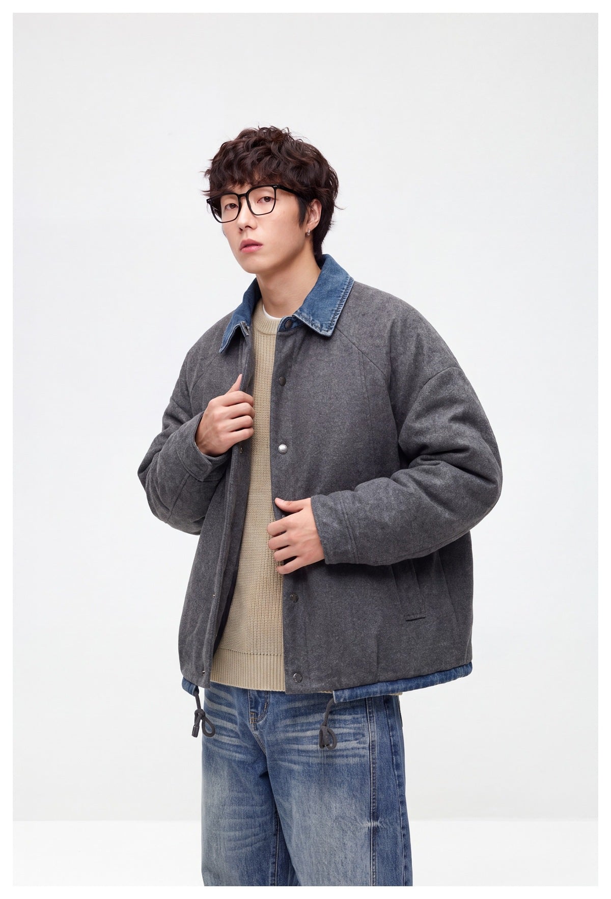 Model holds open a charcoal-gray snap-front jacket with a blue denim collar, showing its front and pockets.