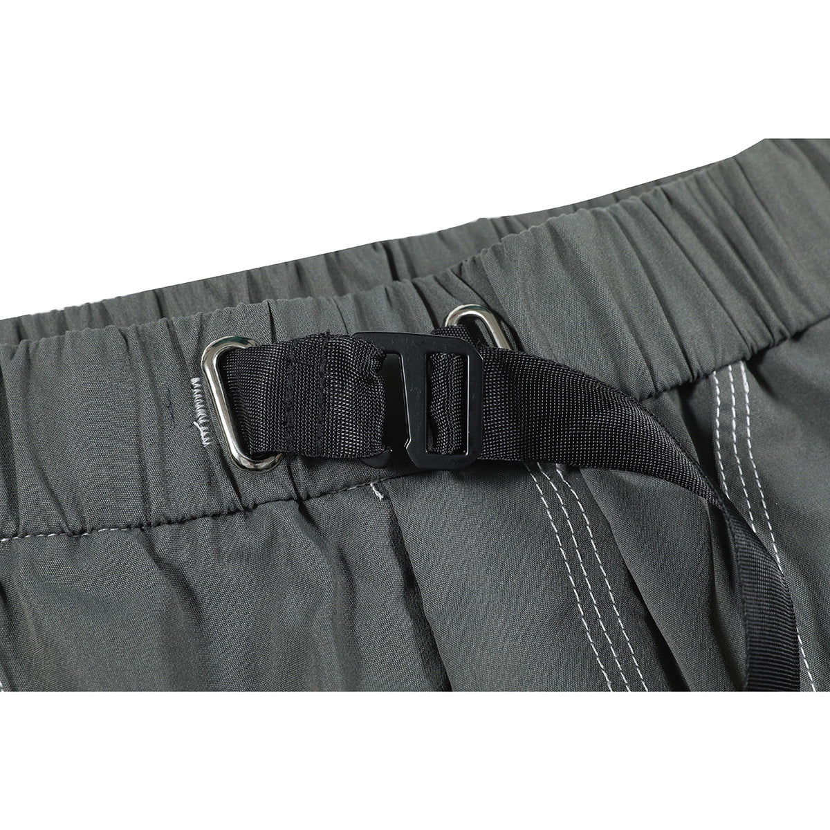 Close-up of charcoal gray pants with a gathered waistband, black webbing buckle and silver metal loops.